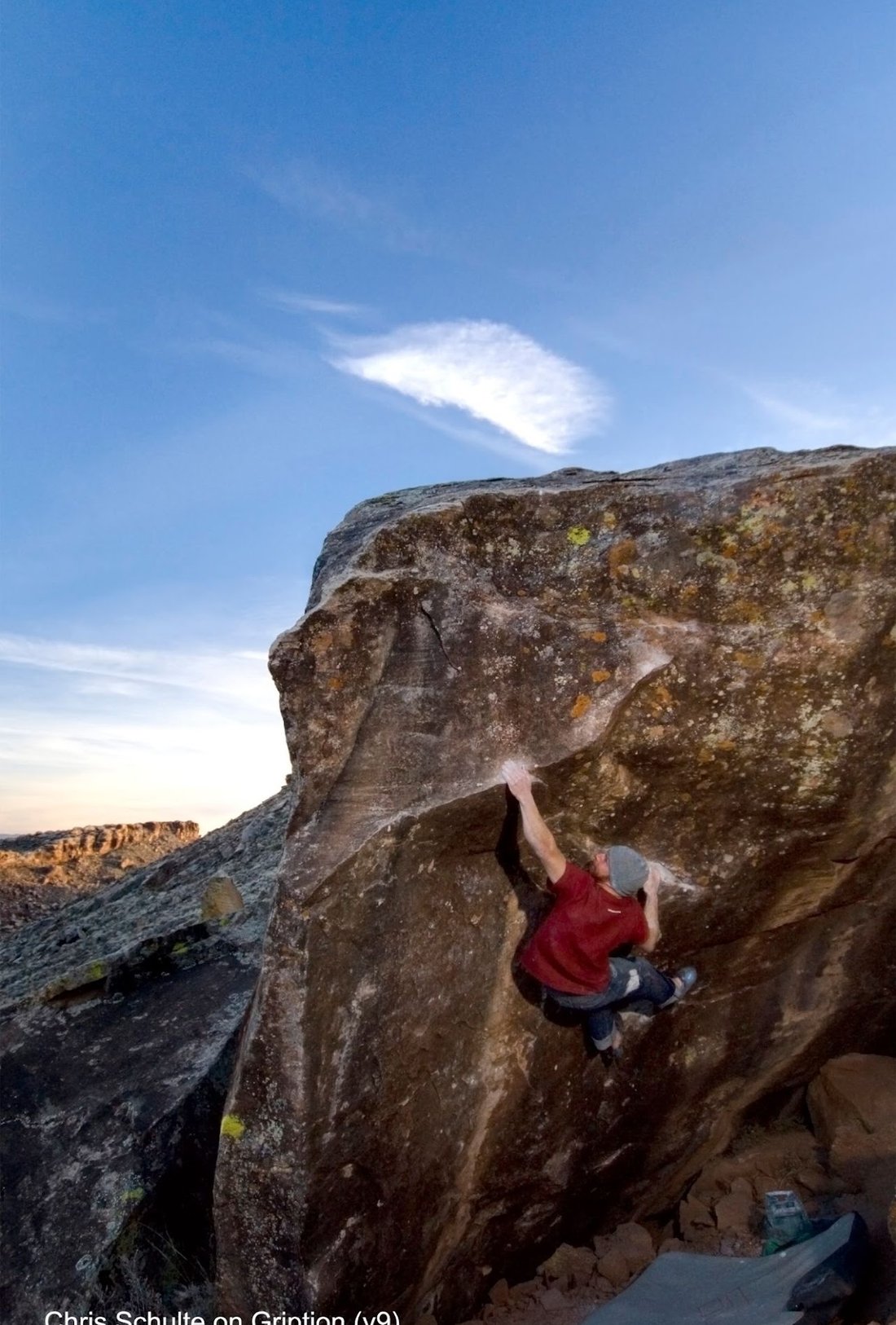 A climber reaching for a high hold on the steep face of Gription at dusk