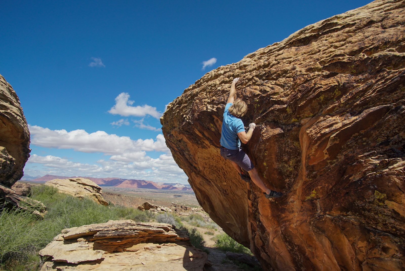 A climber bouldering on a sandstone boulder with the St. George valley and mountains beyond